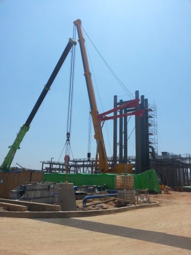 Grúas de construcción levantando estructuras en un sitio de obra bajo un cielo despejado.