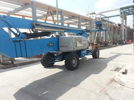 Grúa de brazo articulado azul estacionada en una carretera de construcción.