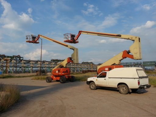 Dos grúas tipo brazos articulados y una camioneta blanca en un sitio de construcción.
